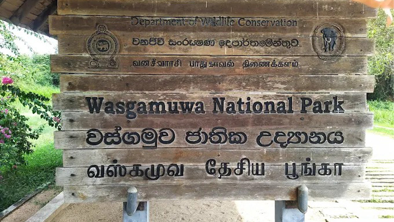 Wooden sign for Wasgamuwa National Park with text in multiple languages.