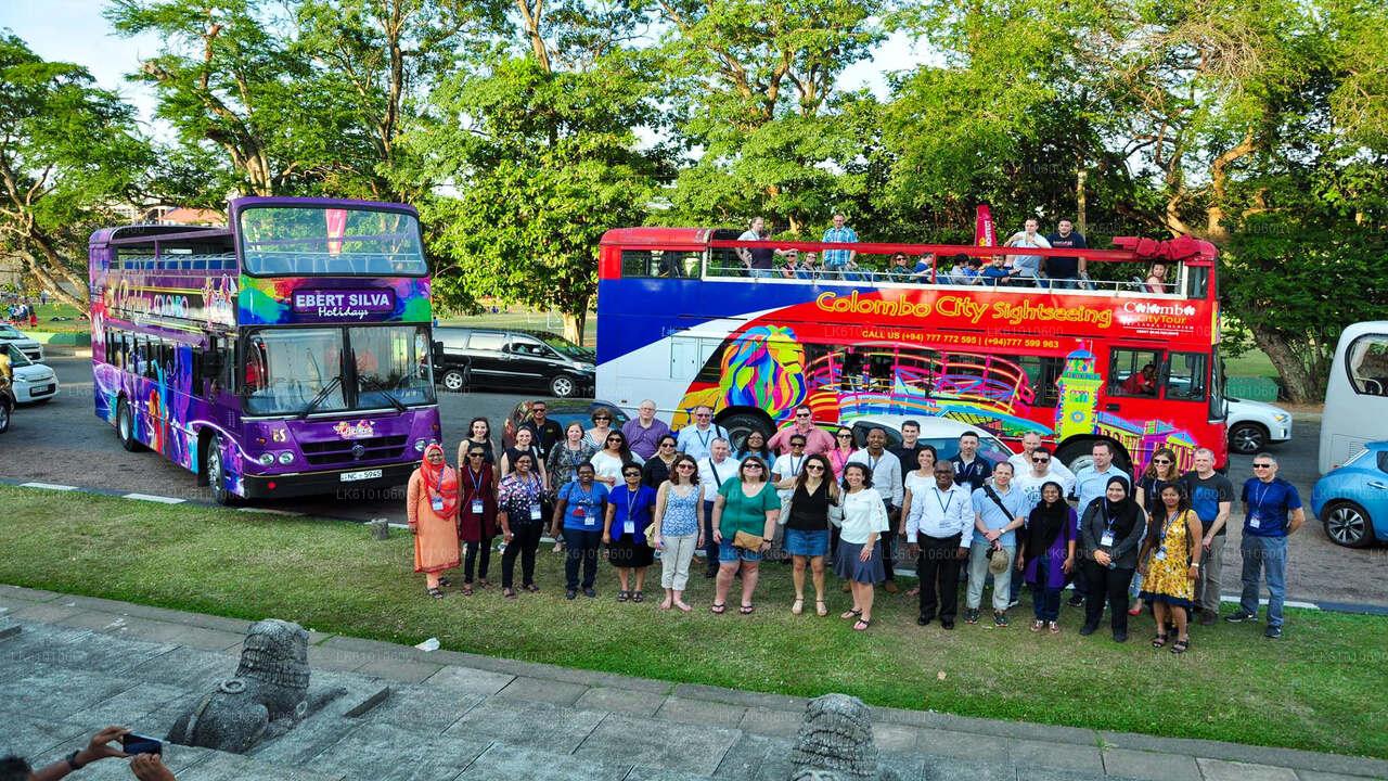 A group of people standing in front of a double-decker open-topped tour bus in Colombo city.